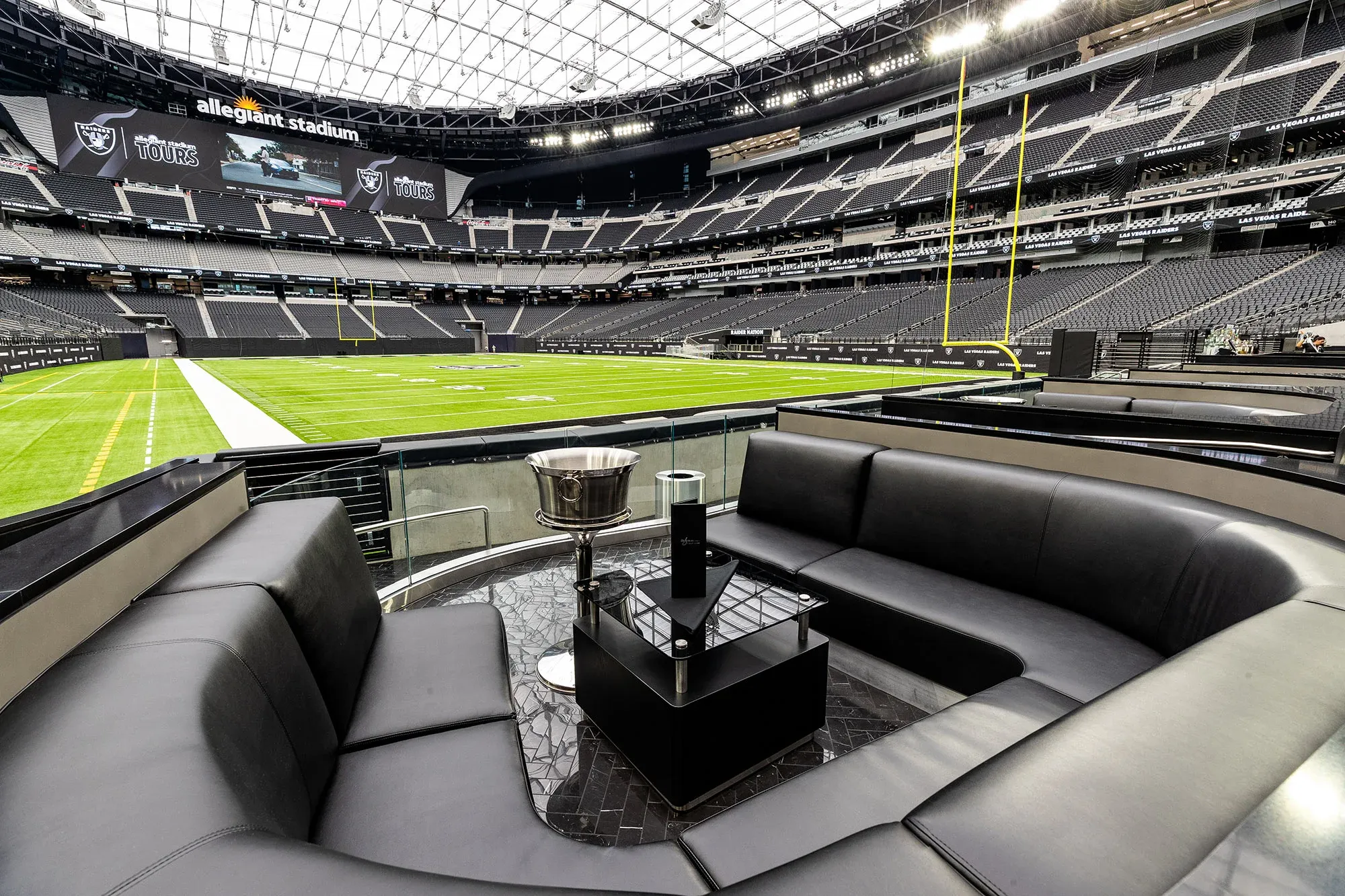 Luxury suite inside Allegiant Stadium with modern black leather seating, a clear view of the football field, and upscale amenities. Emphasizes the premium gameday experience for fans and corporate guests.