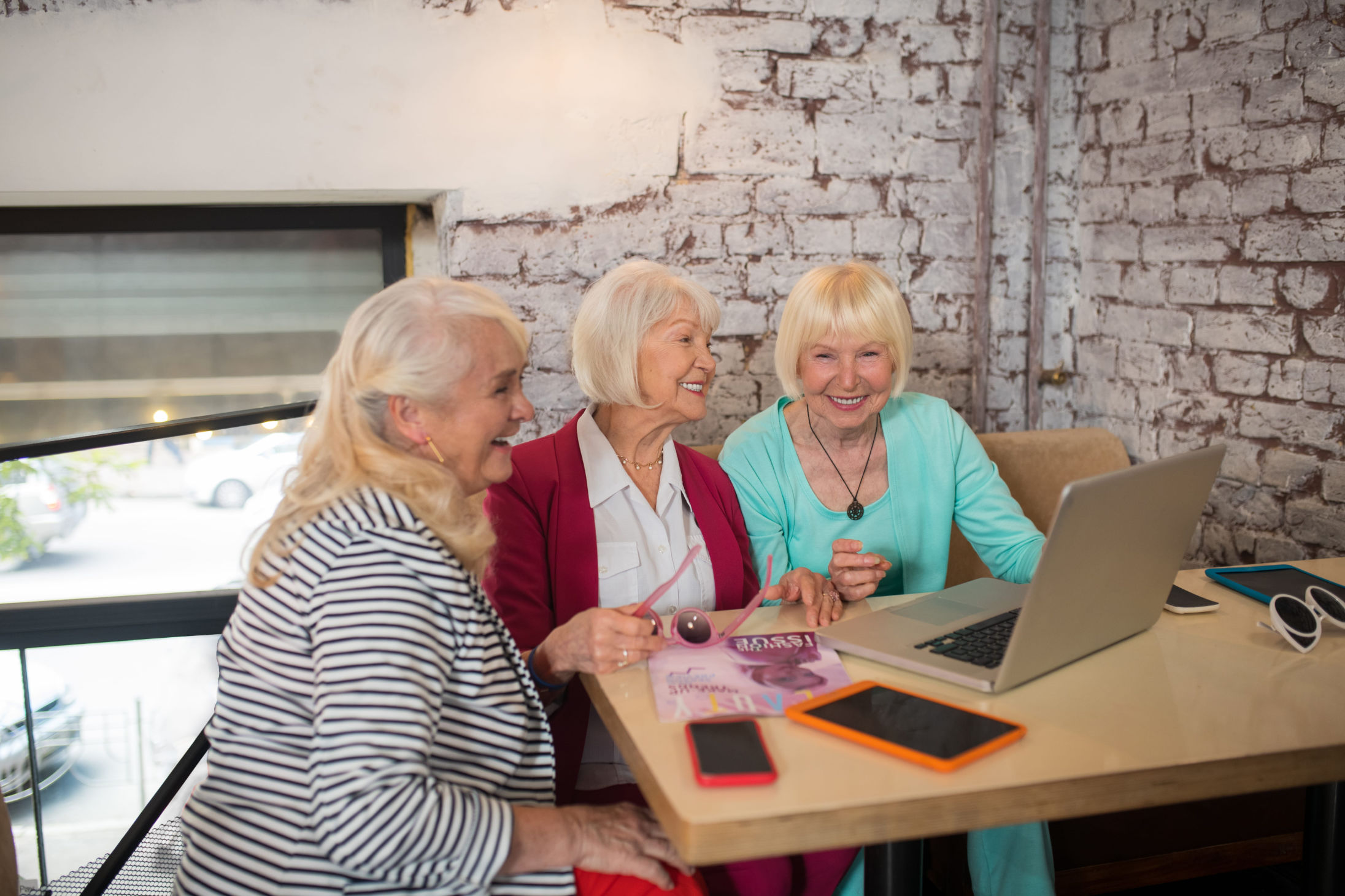 Eine Gruppe von drei Senioren, die gemeinsam Laptops und Smartphones nutzen.