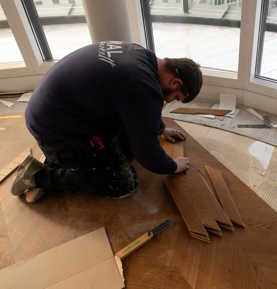 Bodenleger passt Chevron-Parkettelemente präzise an und verlegt sie sorgfältig im Innenraum.