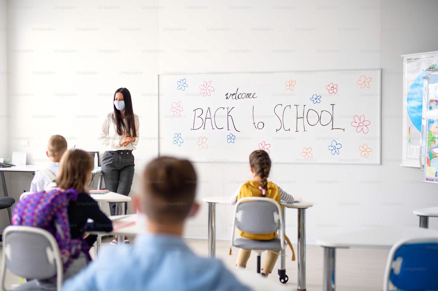Classroom with students and teacher, wearing masks, back-to-school welcome, education setting.