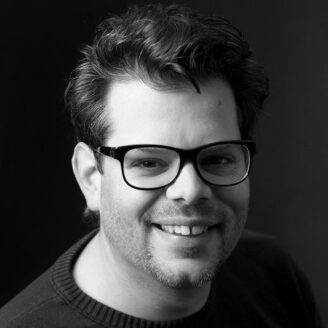 A person wearing glasses and a sweater smiling.