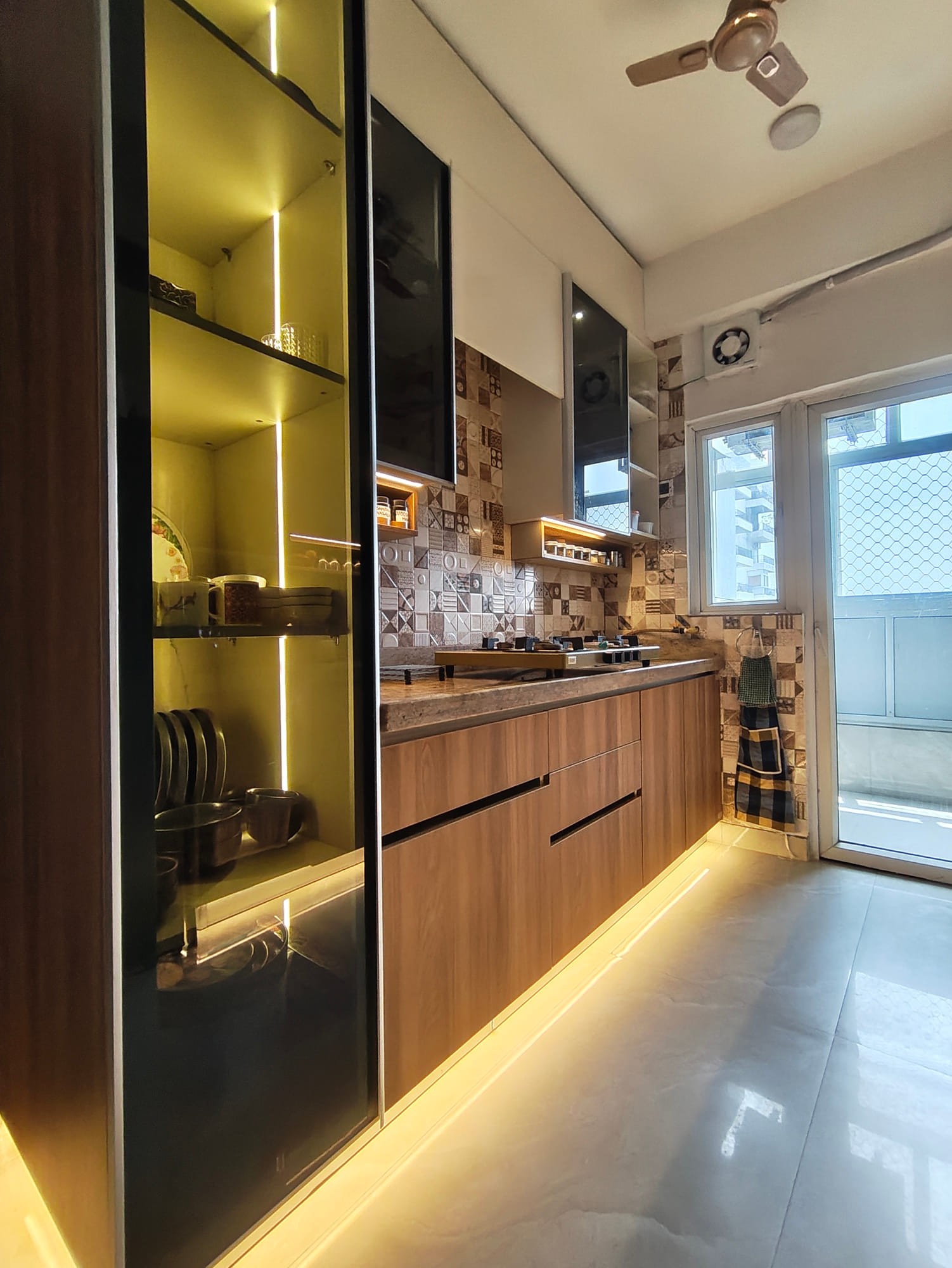 Backlit glass-fronted tall unit in dark wood beside the granite worktop, looking down the galley kitchen