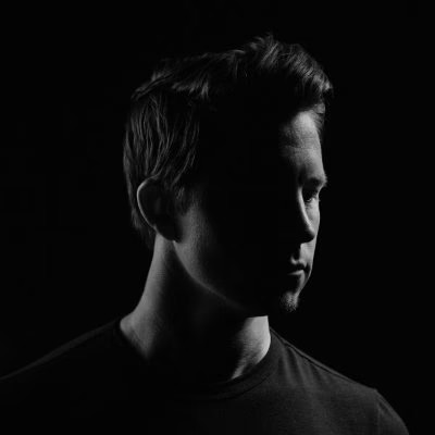 Portrait of a young man with long hair and a beard, wearing a black hoodie.