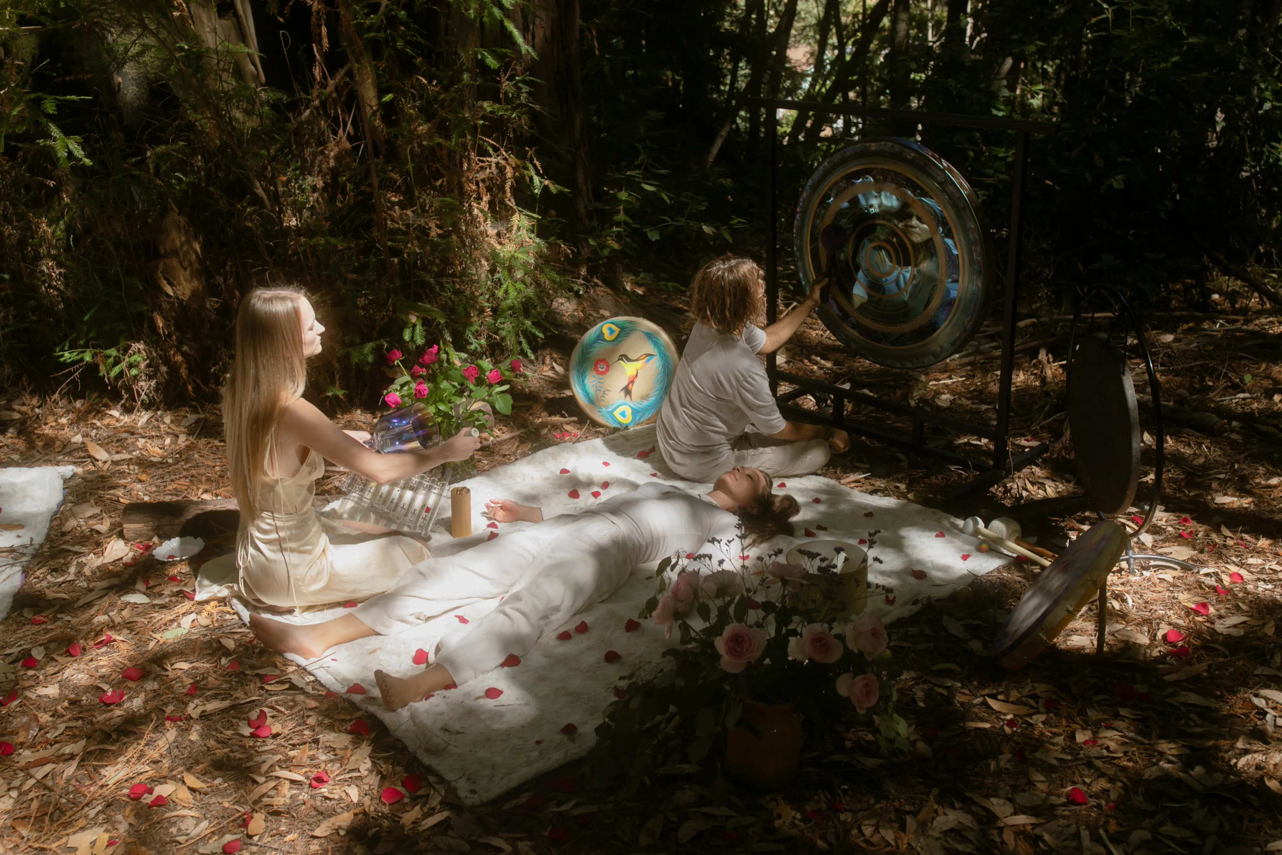 Two women in sacred ceremony outdoors surrounded by rose petals and ceremonial objects