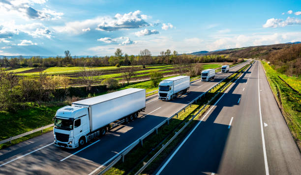 image of multiple large haulage trucks transportinmg goods along a road with feilds either side