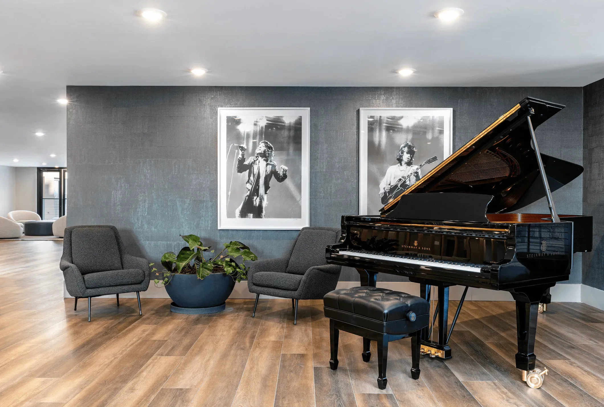 A stylish interior featuring a grand piano, two chairs, and framed artwork on a gray wall with wood flooring.