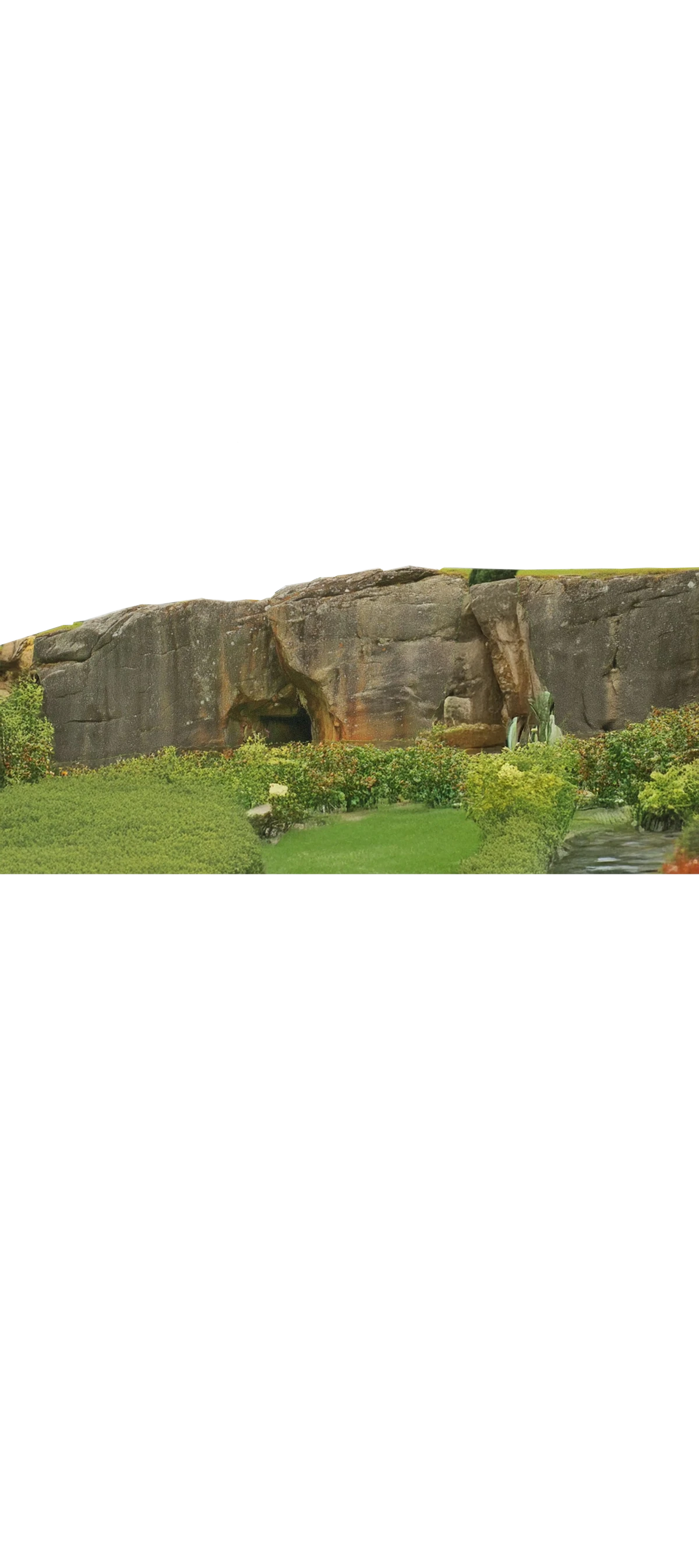 Large horizontal rock formation surrounded by carefully maintained vegetation, blending raw stone and garden design.