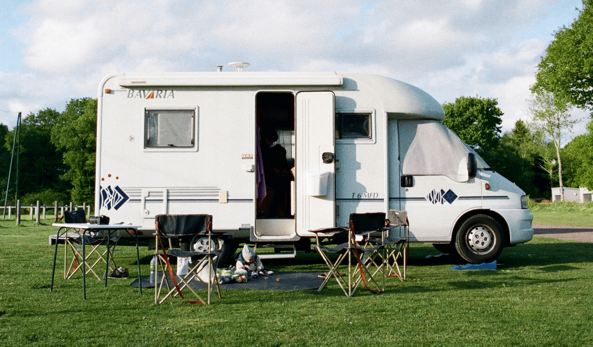 white and brown rv trailer on green grass field under white cloudy sky during daytime
