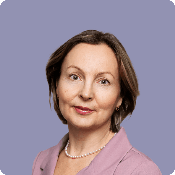 A brown haired, serious looking woman in a pink blazer in front of a purple background.