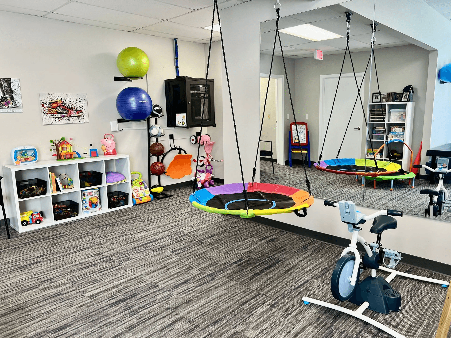 Children's therapy room at Advantage Physical Therapy featuring a sensory platform swing, climbing wall, and colorful developmental murals.