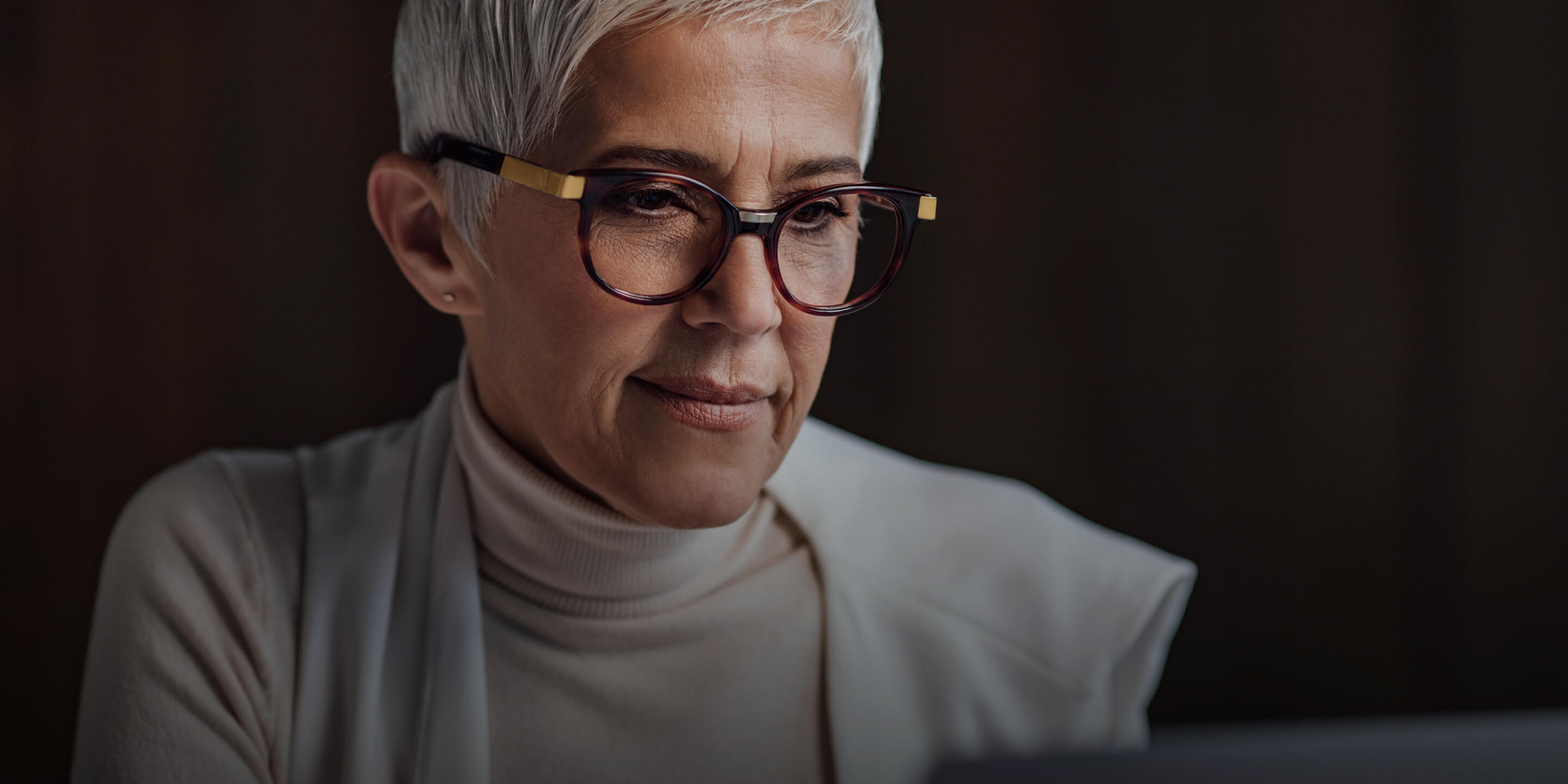 Older woman with glasses looking down at a laptop