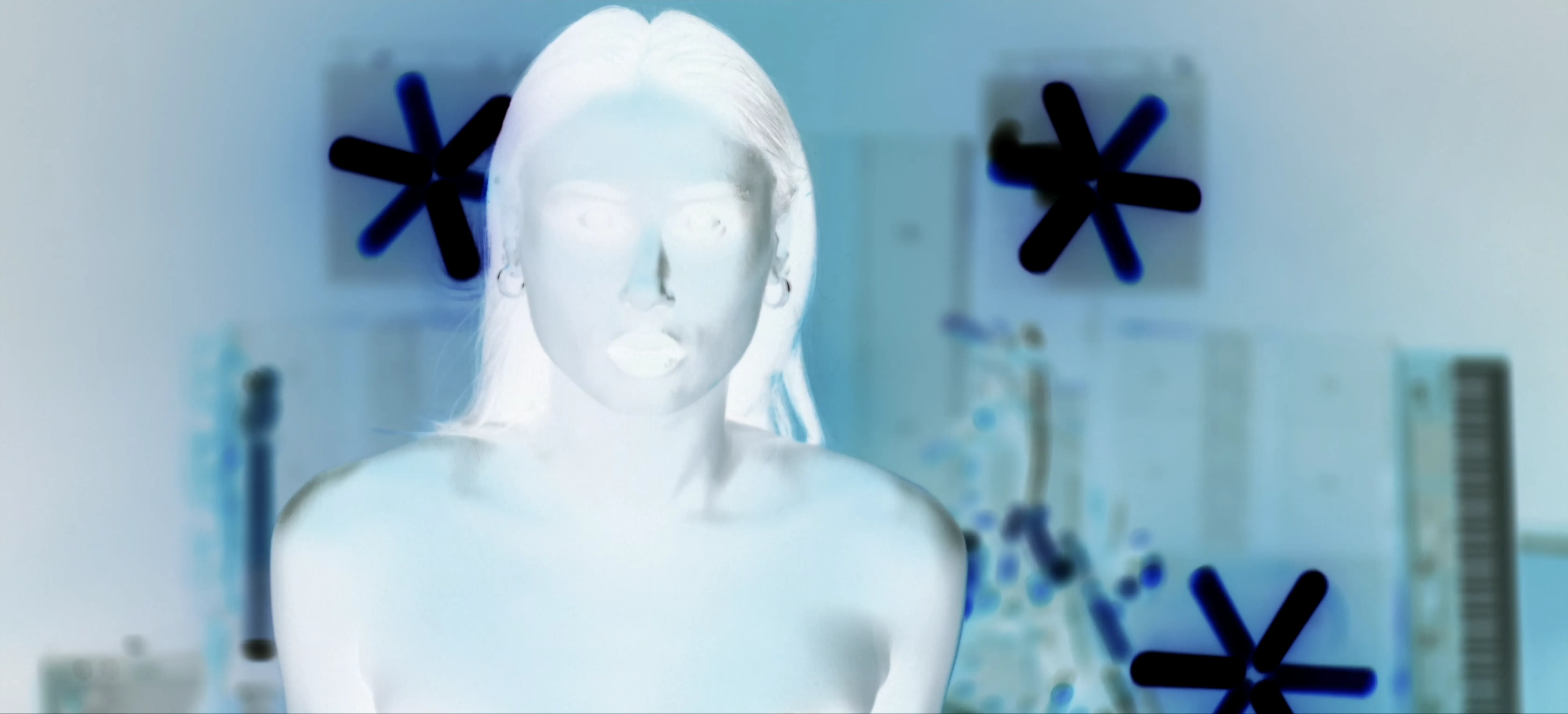 An abstract image with a high-contrast, inverted color scheme features a silhouetted person in the foreground, surrounded by large, dark star-like symbols, set against a blurred background of various shapes and patterns, creating a mysterious and artistic visual effect.