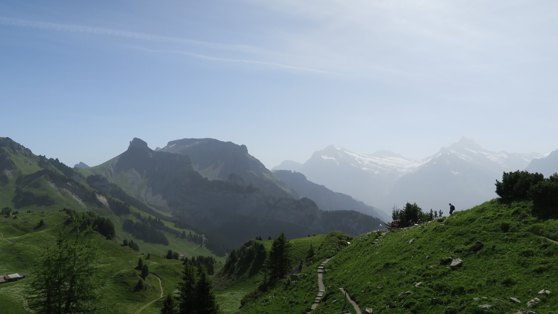 Mountain path with hikers on Schynige Platte, Switzerland, overlooking alpine peaks and green valleys.