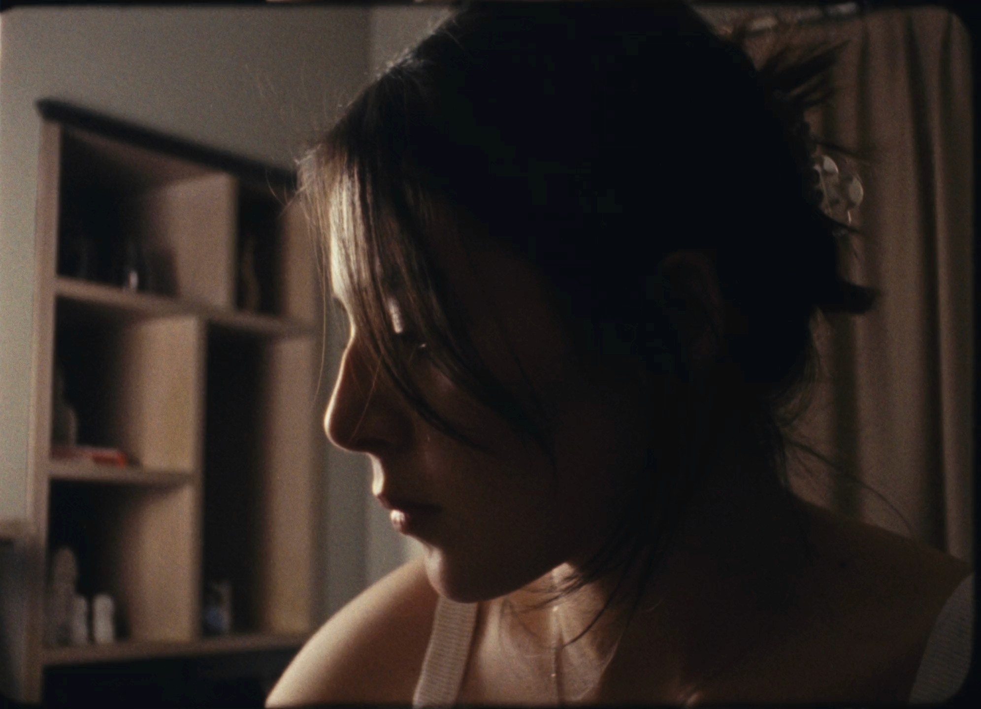 A raw 16mm film still from the documentary project 'Alla Prima,' photographed by Mexico City DP Mauricio Nader. The shot, captured on KODAK VISION3 250D film with a Bolex H16 camera, features a woman in natural light painting a self-portrait, showcasing organic grain and texture.