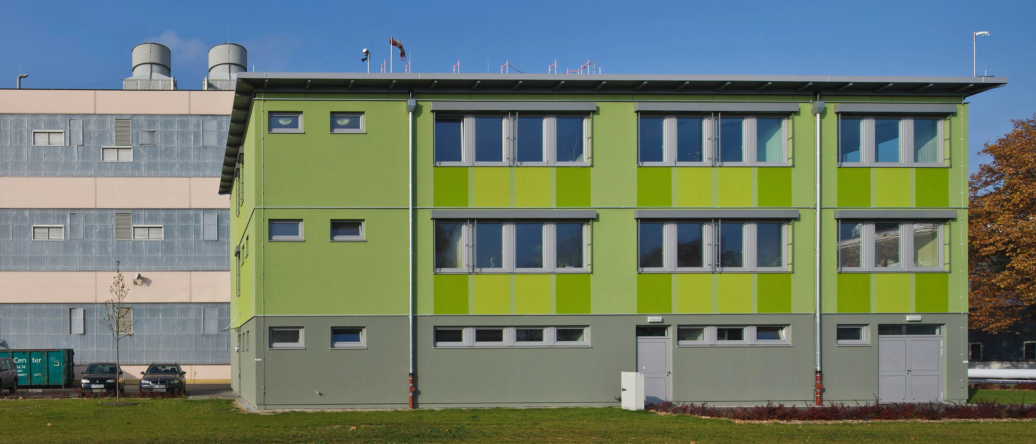 Mehrstöckiges Gebäude in hellgrüner und dunkelgrüner Farbgebung mit mehreren Fenstern und zwei Eingängen.