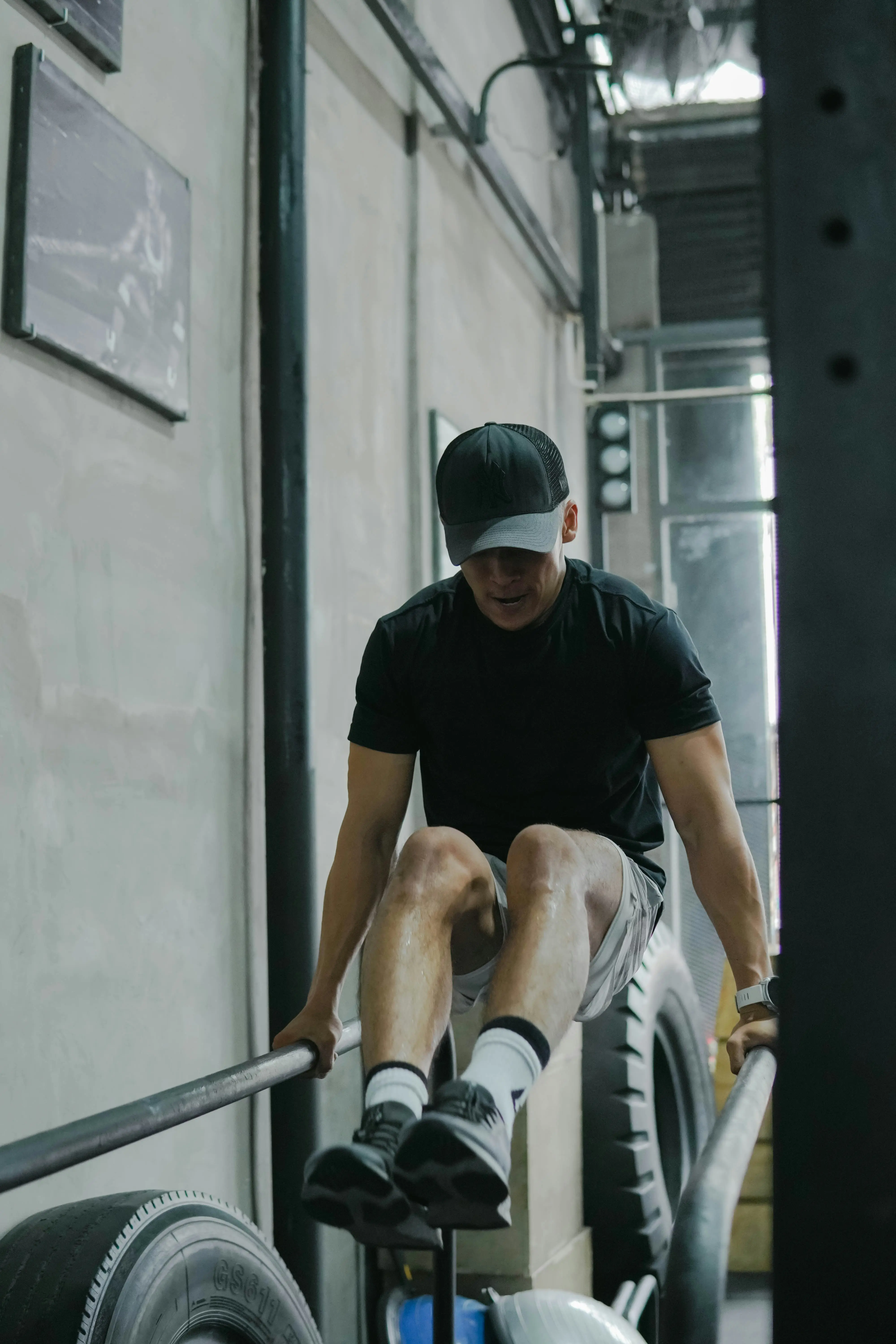 Athletic man performing an L-sit hold on parallel bars inside an industrial-style gym.