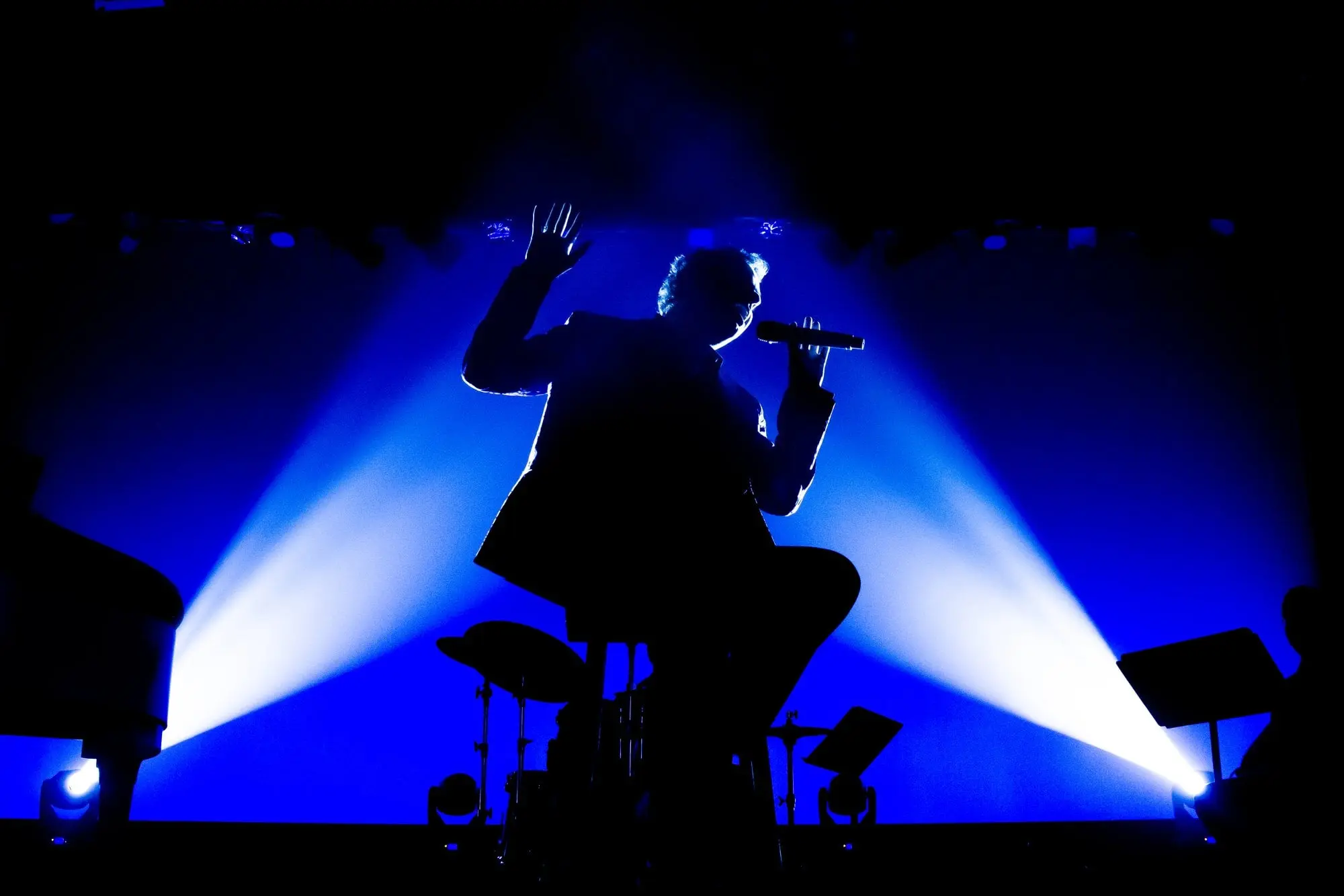 A silhouette of a performer holding a microphone is dramatically highlighted against a vivid blue, backlit stage at the Manatee Performing Arts Center in Bradenton, FL.