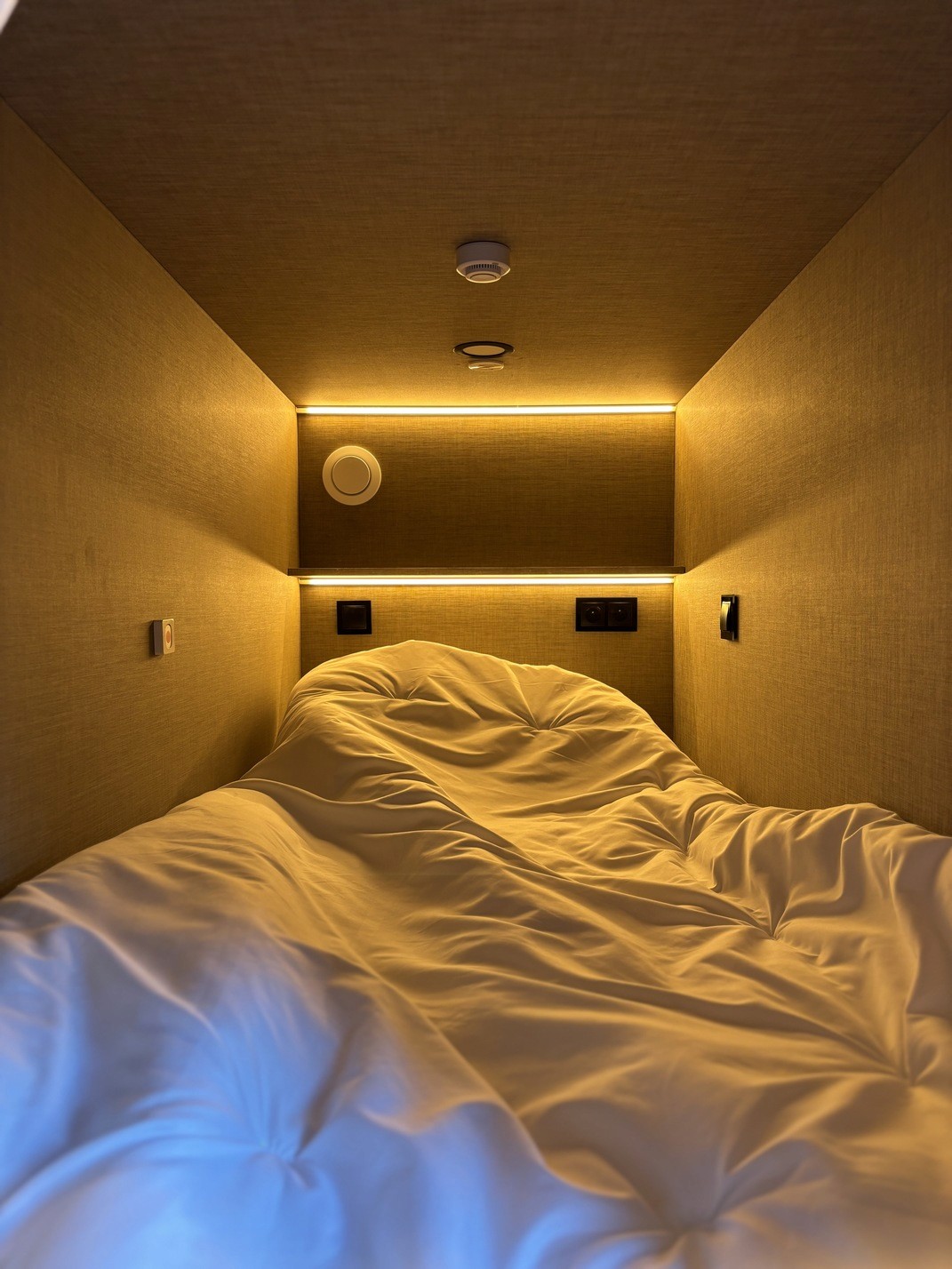 Cozy bedroom with a bed, shelf with books and diffuser, and a warm, inviting atmosphere.
