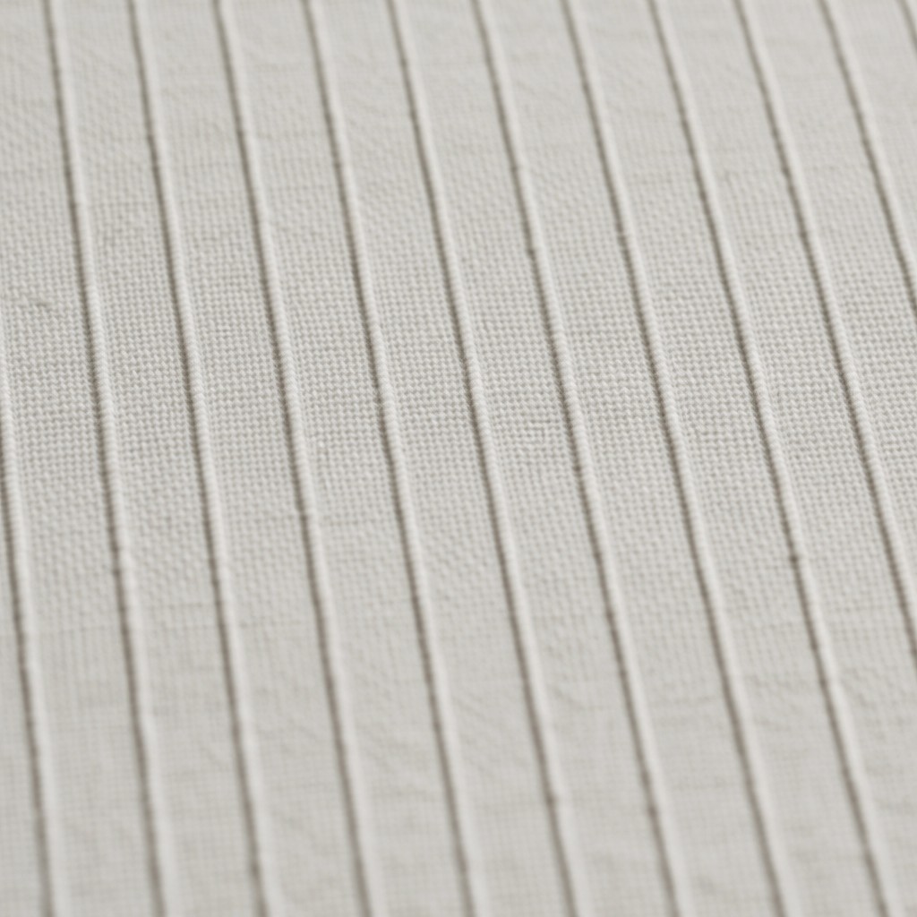 A macro shot showing the detailed texture of off-white pleated fabric. The parallel vertical ridges create a clean, minimalist pattern across the frame.