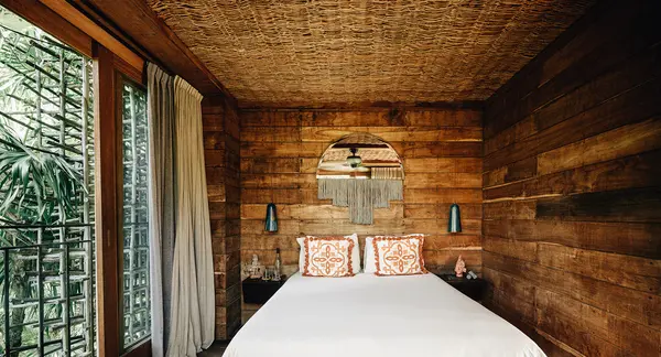 Treehouses at Nômade Tulum highlighting spacious bed with pillows and cushions, 2 lamps, and large mirror.