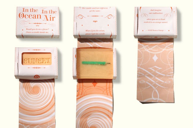 Three boxes of candles are displayed against a white background. The leftmost box is labeled “Sunset” and features a peach-colored design with concentric circles. The center box is open, revealing a green candle inside. The rightmost box is closed and displays a peach-colored design with decorative lines and shapes. All boxes have text on the top, including “In the Ocean Air” and “The candle and I are different, yet the same.”