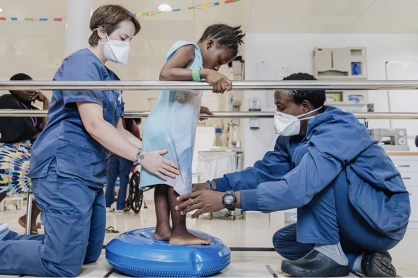 Two volunteers helping a young girl stand up