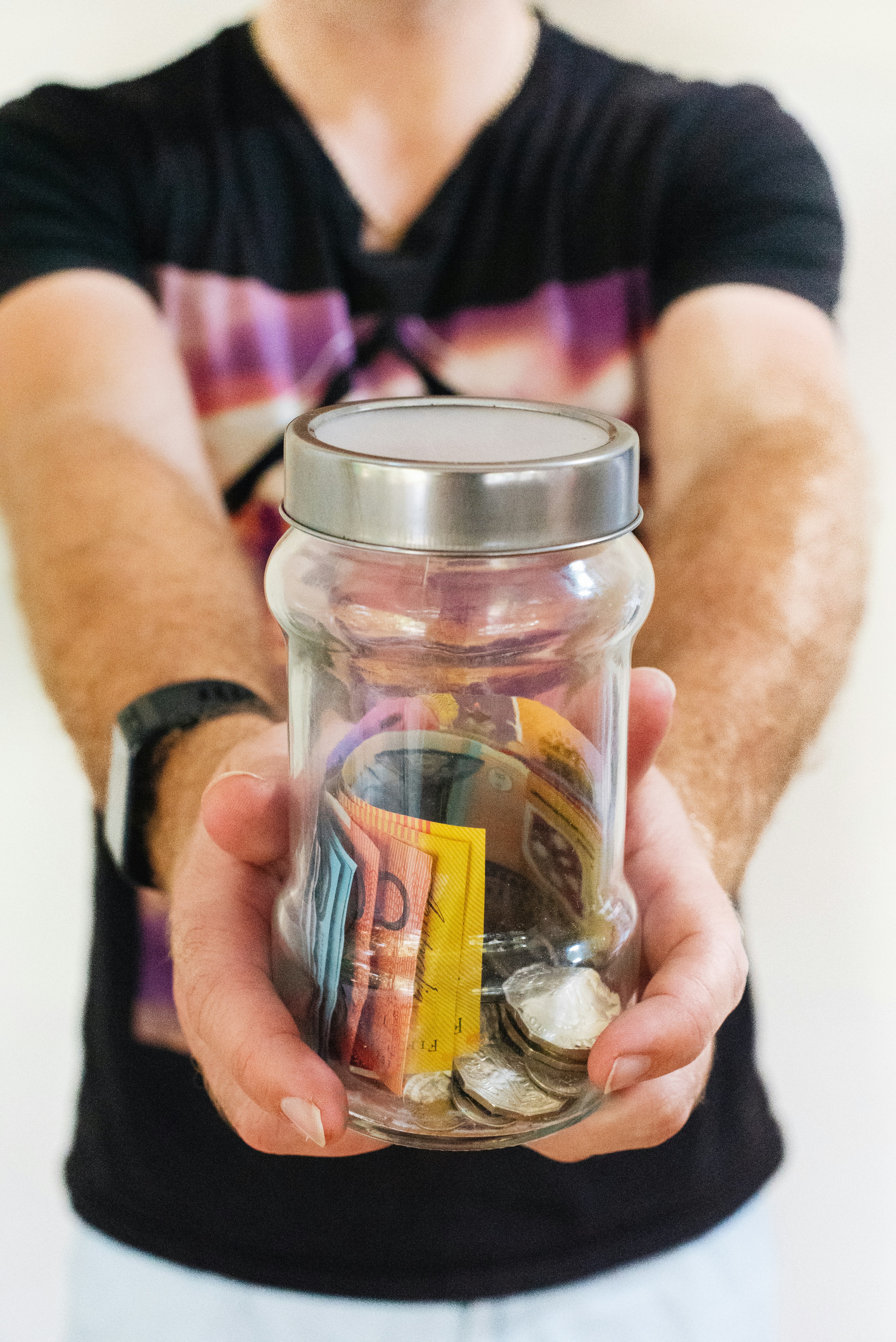 man holding clear glass jar of money