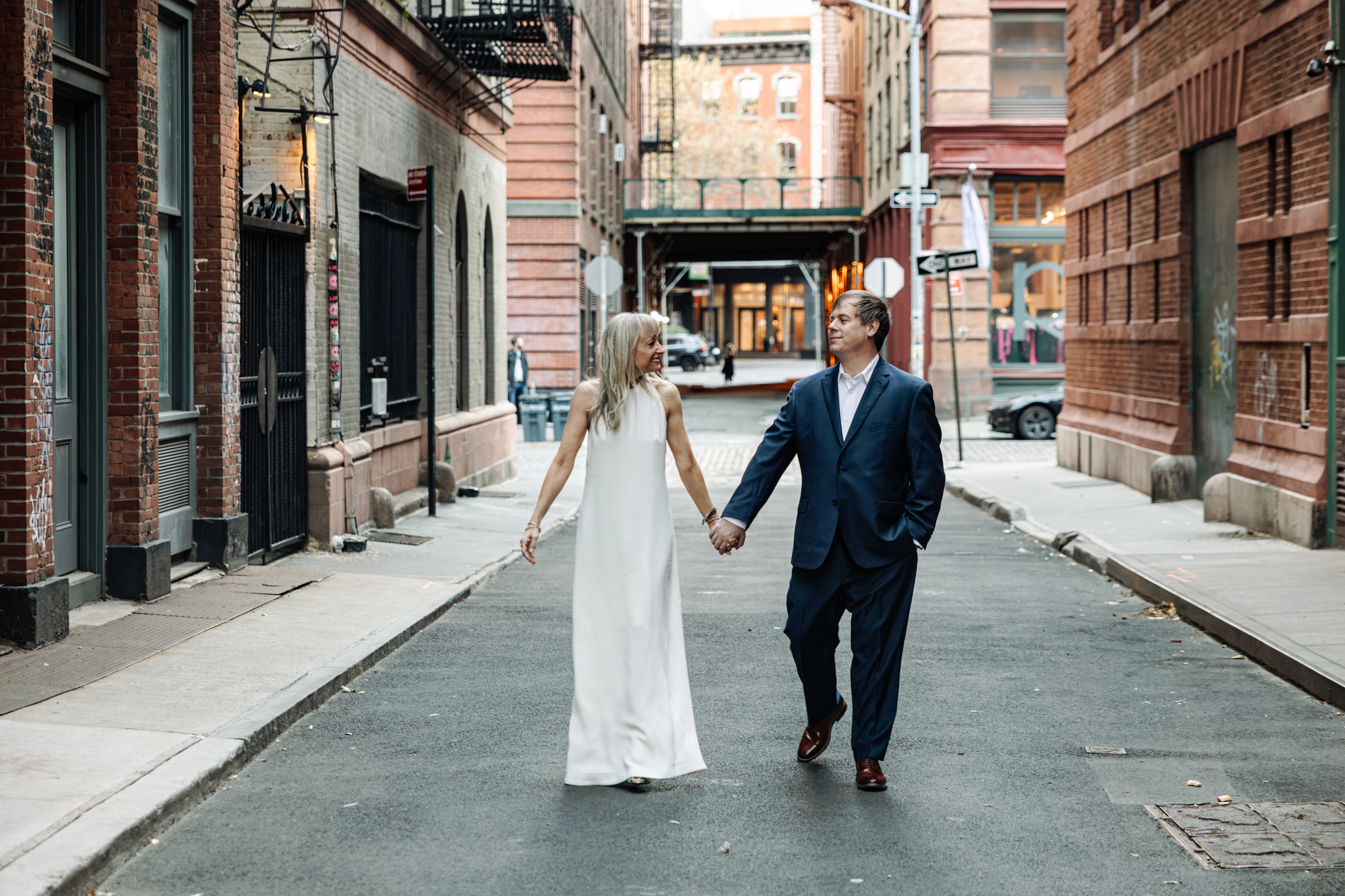 Couple walking hand in hand toward the camera, eyes locked on each other, beneath the iconic Staple Street Bridge in Tribeca, NYC — effortlessly cool couples and wedding vow renewal photography by Lizz Spano Photography, New York City couples photographer.