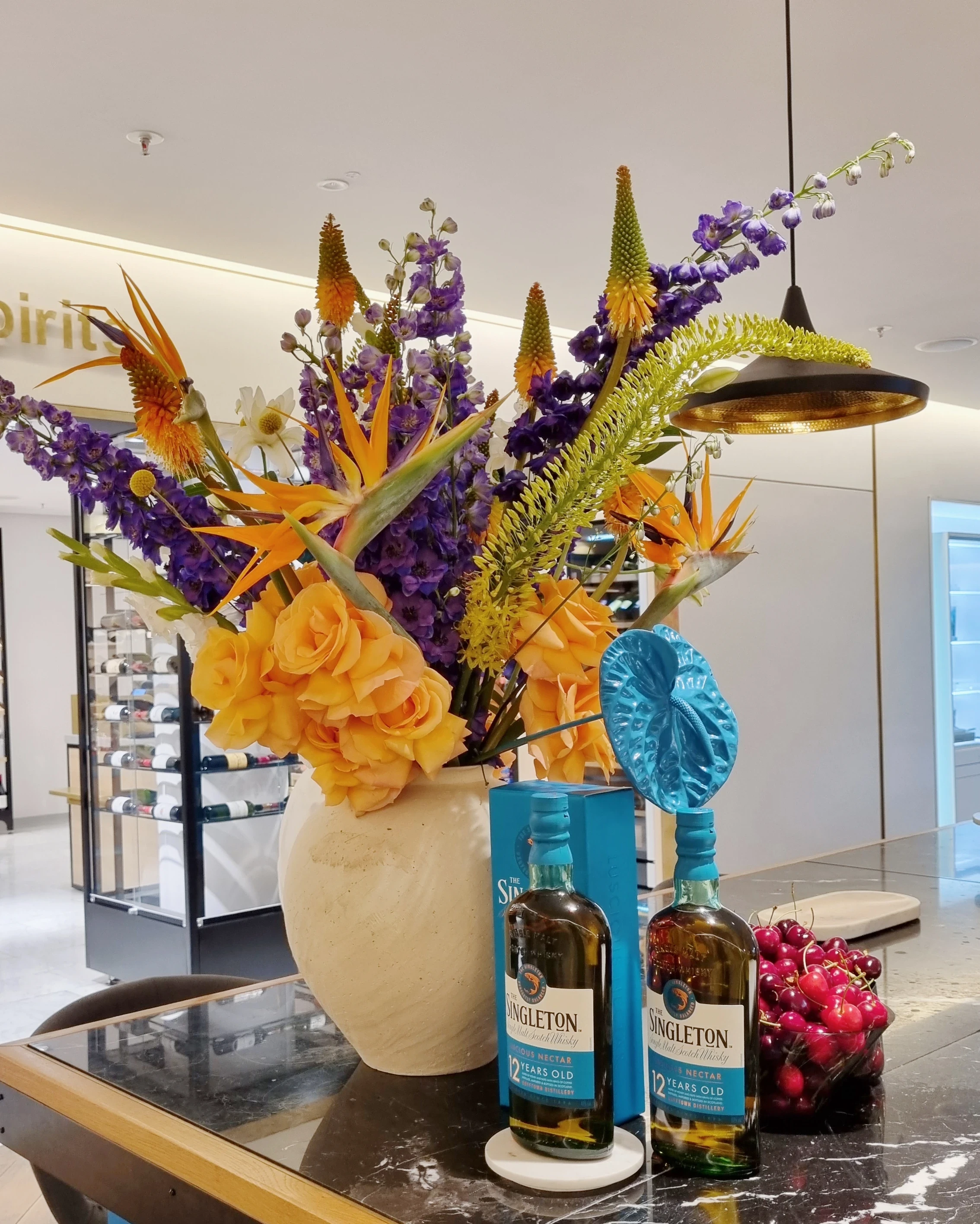 Lavish bouquet with strelitzias next to Singleton bottles, blue rosette and red grapes.