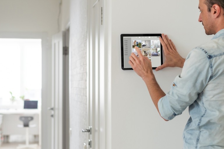 Personne regardant une tablette fixée sur un mur, avec des projections provenant de caméras de surveillance.