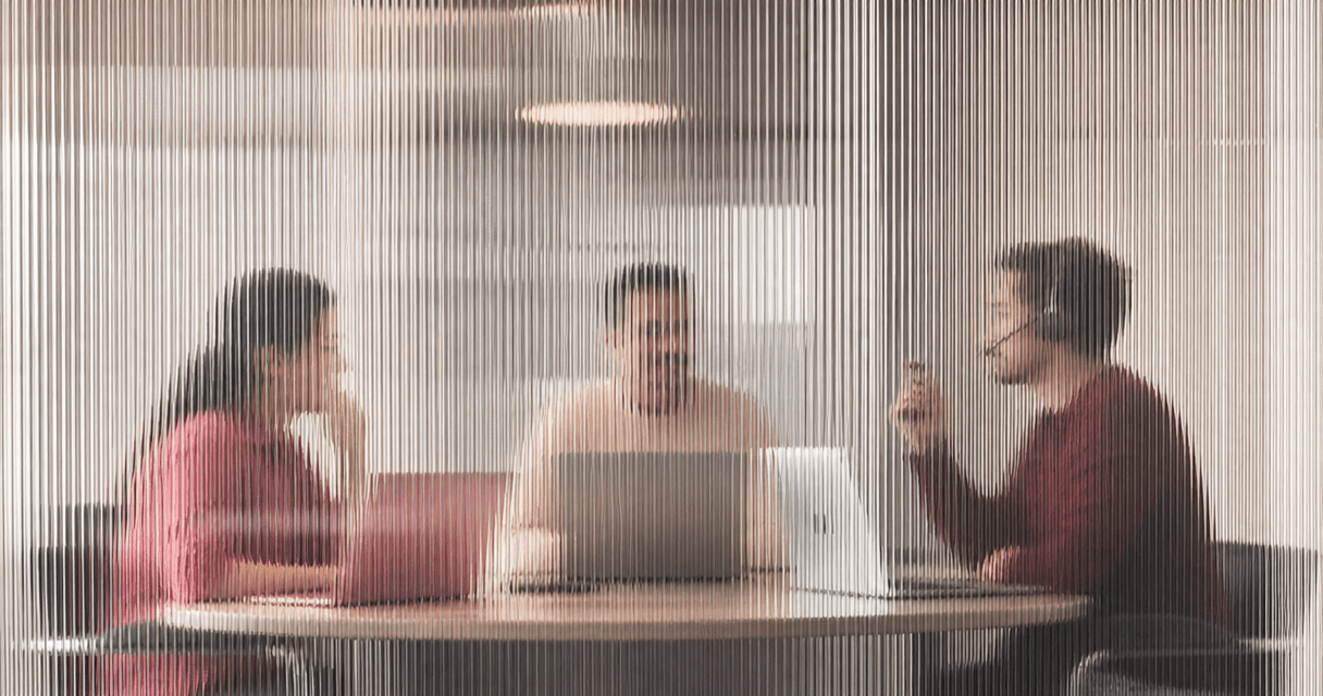 Sales team collaborating around a table, one member on a headset call, seen through vertical fluted glass