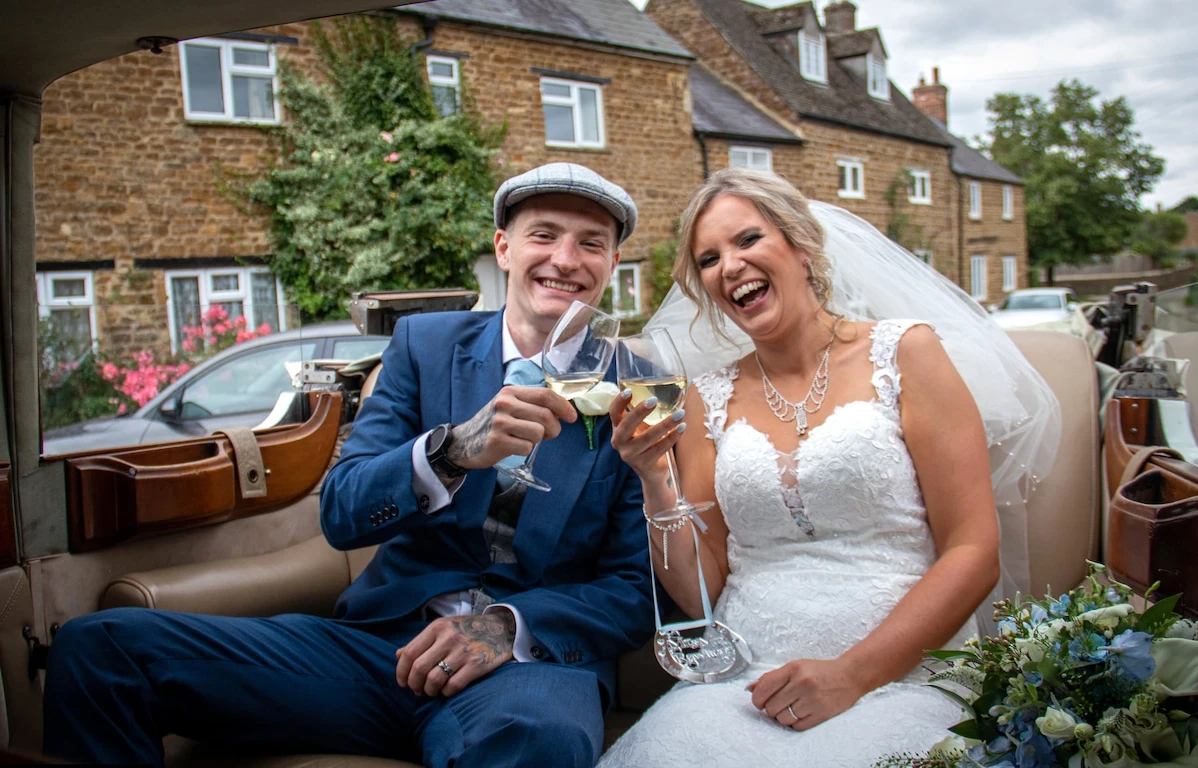 Bride and groom celebrating with champagne in a vintage car on their wedding day