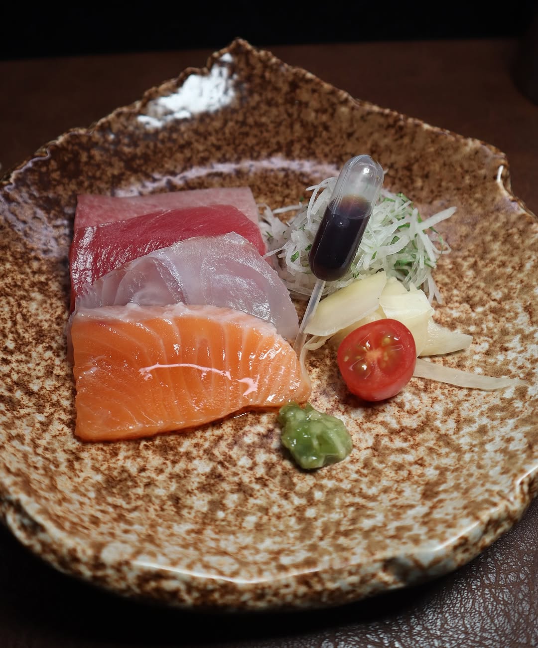 A beautifully plated sashimi dish at Toka Chef, showcasing fresh salmon, tuna, and yellowtail with wasabi, soy sauce, and a touch of greenery for garnish."