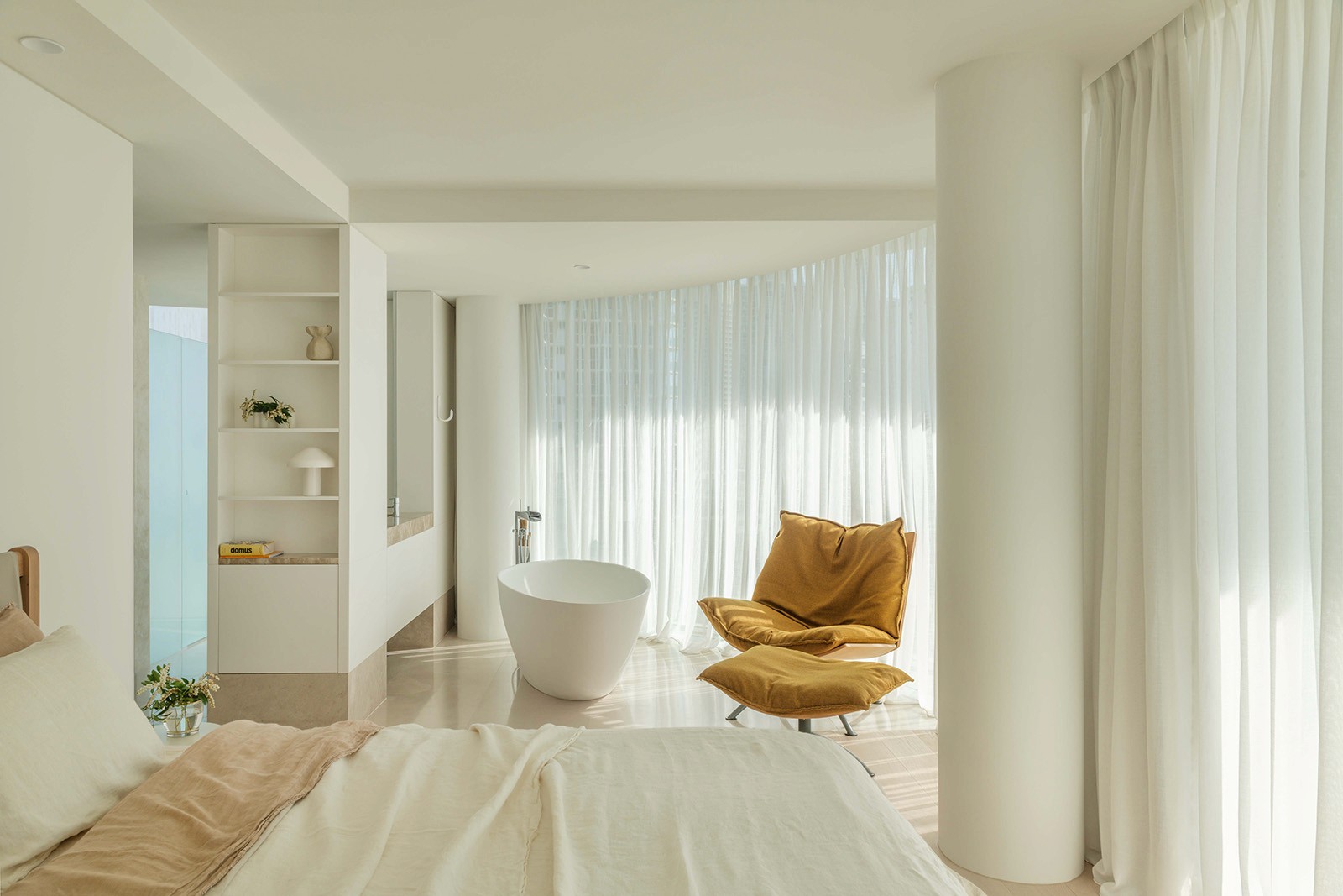 High Tide apartment bedroom suite with freestanding bath, sheer curtains, sculptural lounge chair, and soft coastal interior design.