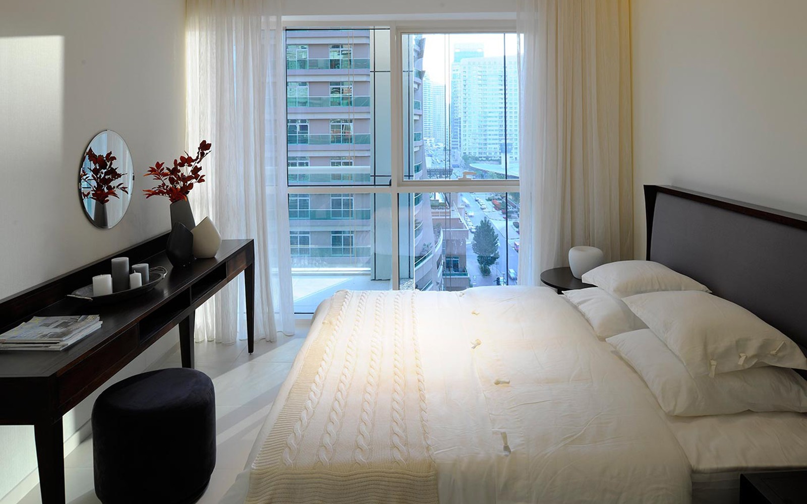 A bedroom in West Avenue Tower featuring a bed, a desk, and a window with natural light streaming in.