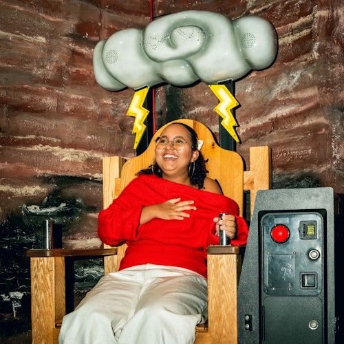 一个人坐在装饰有闪电图案的木椅上，头顶有云朵构造，微笑着，手握一个杠杆。