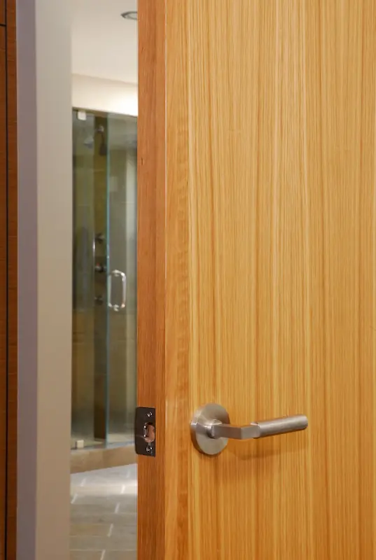 Wooden door ajar with stainless steel handle, glimpse of modern bathroom. For Irvine Transitional Modern, photo by Chris Darnall.
