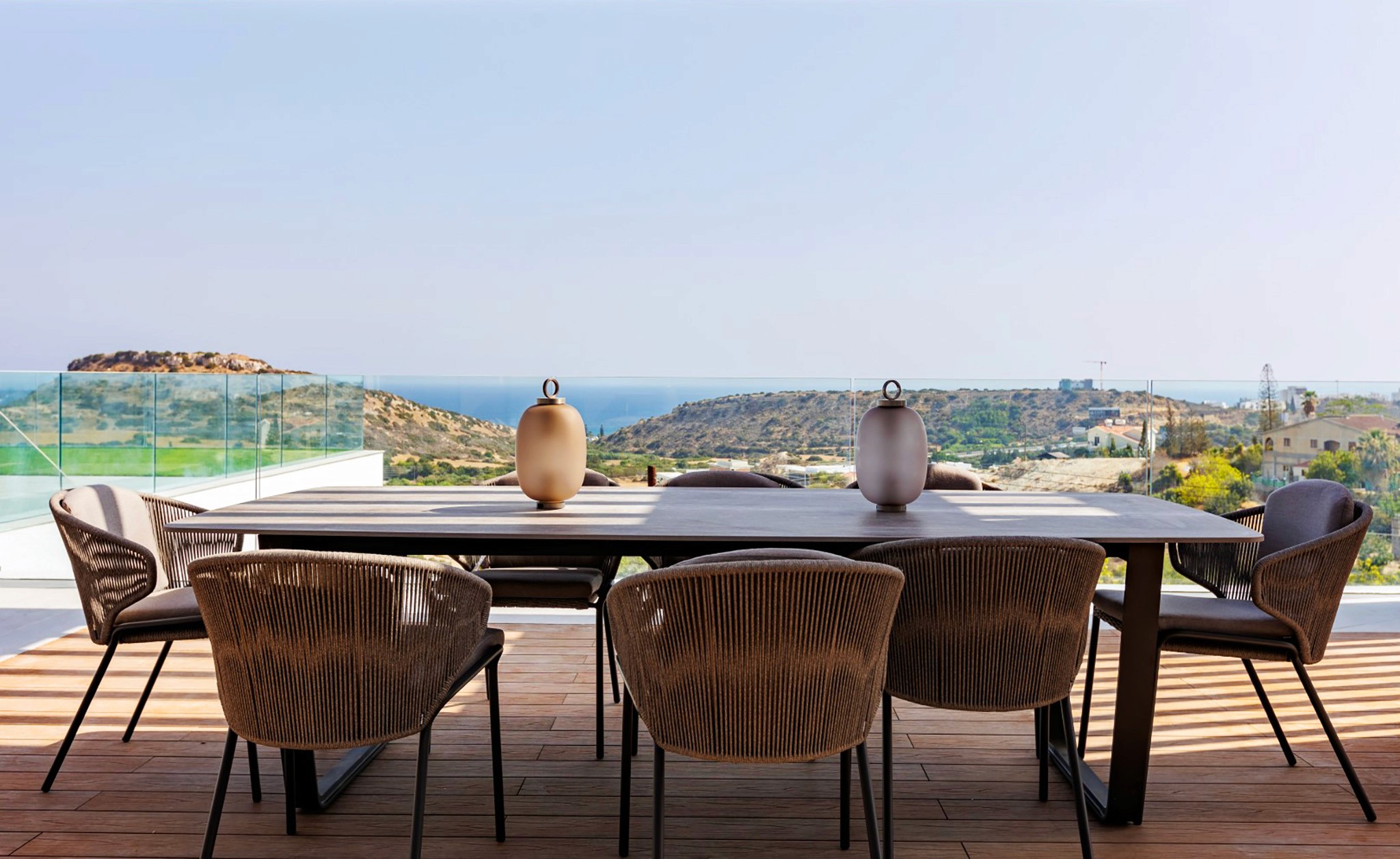 Villa Trio outdoor dining terrace with woven chairs, long table setting, and sea-view panorama