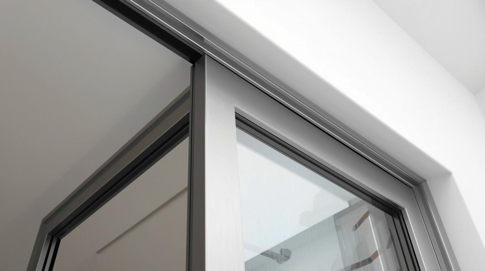 A sleek, modern aluminium sliding door, viewed from a slightly low angle, showcasing its brushed metal finish and clean lines. The framing is minimalist, emphasizing the door's structure.