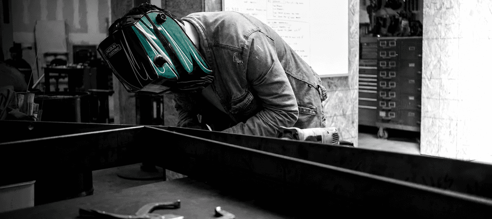 Metal fabrication in the Digital Foundry workshop, with a fabricator wearing a teal welding helmet.