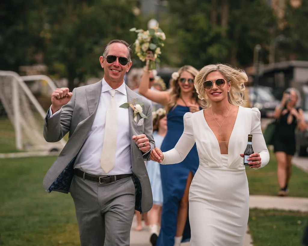 Newlyweds walking across a lawn with drinks in hand