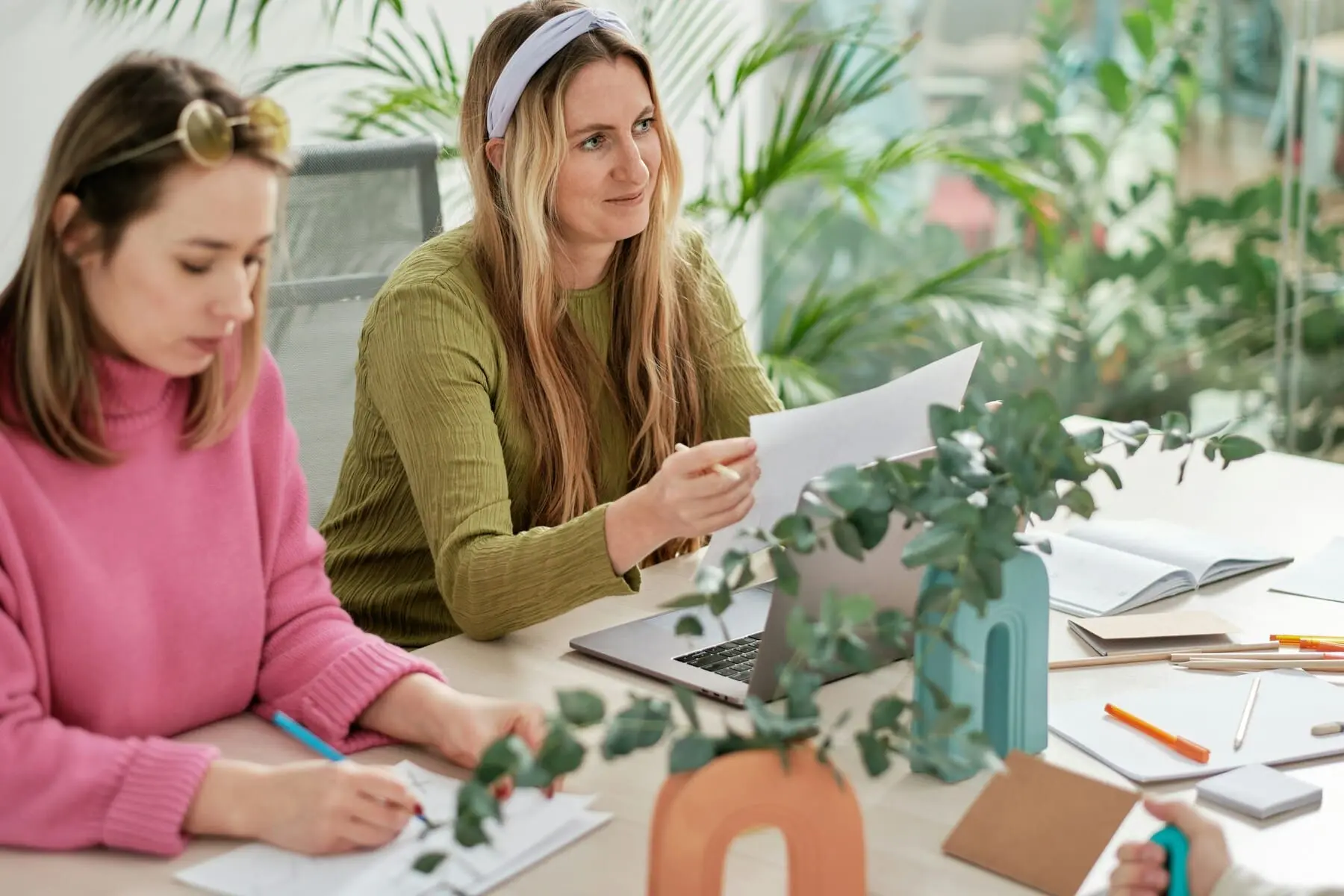 Woman sitting with a group of women, looking happy and positive while discussing something over a laptop.