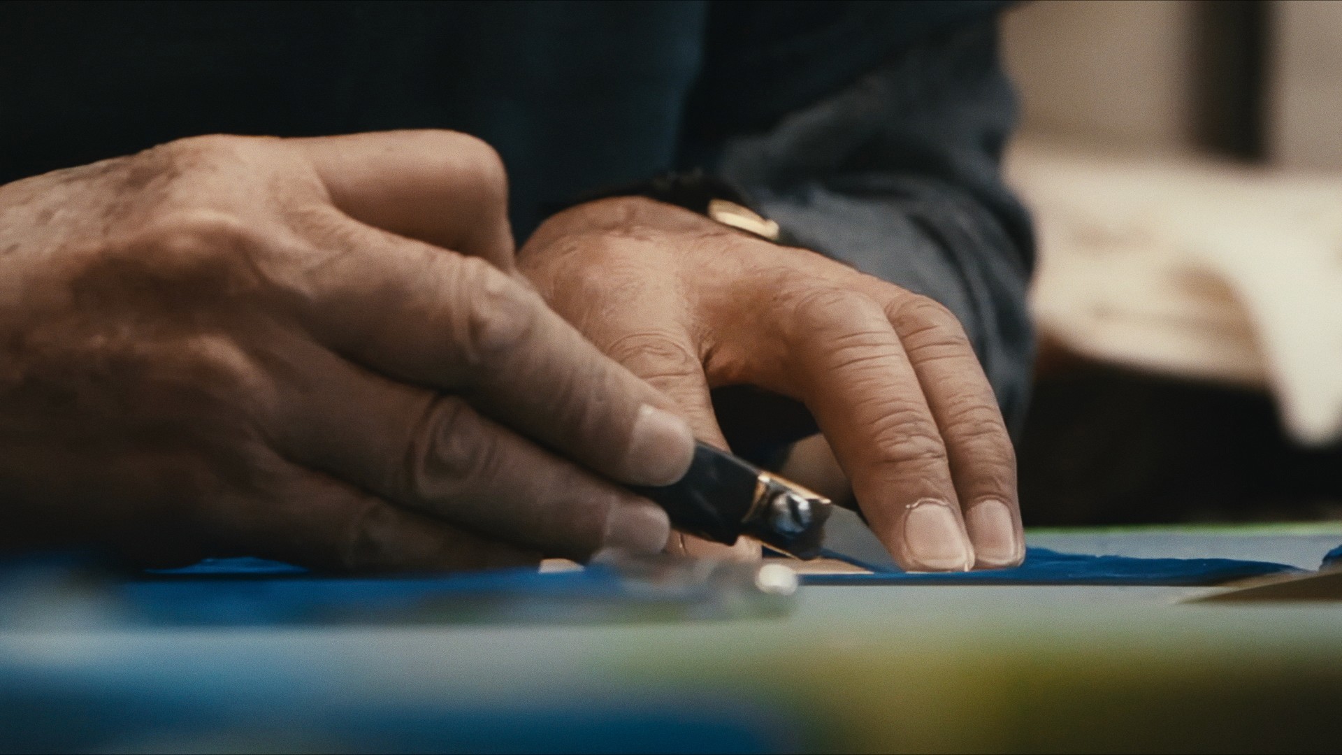 Hands cutting leather on a blue workbench, Maddman