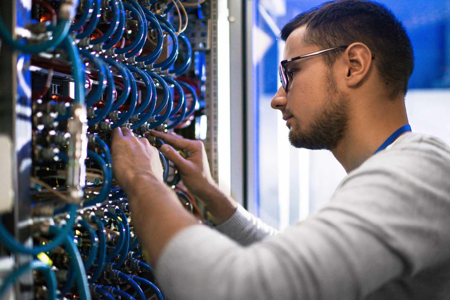 Engenheiro de redes com óculos configurando cabos e conexões em rack de servidores, representando gestão de infraestrutura de TI e cabeamento estruturado em data center - FindUP - manutenção preventiva e corretiva