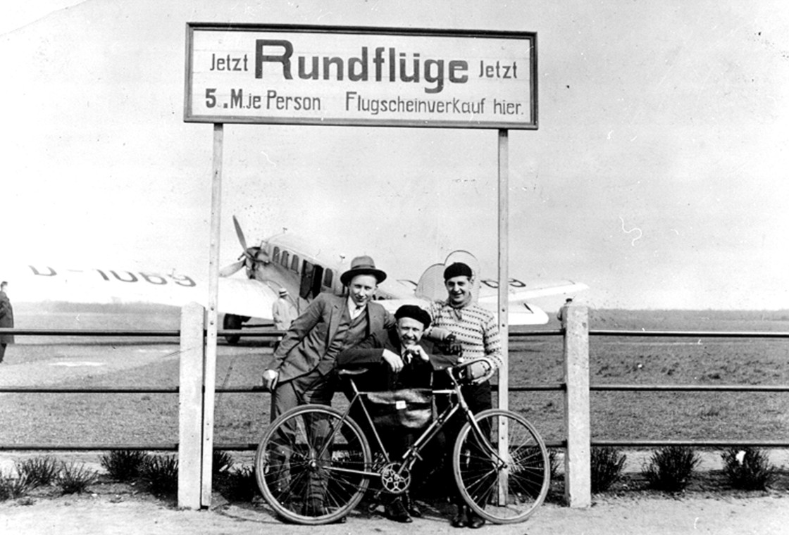 Menschen stehen mit Fahrrad vor Schild für Rundflüge am Flugplatz Dortmund