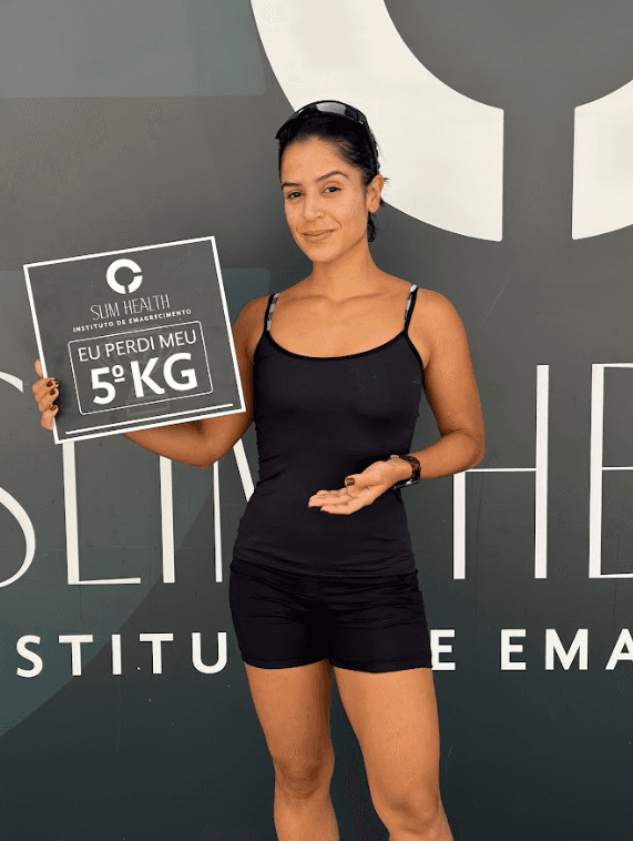 A smiling young man with crossed arms, wearing a plaid shirt and white t-shirt, poses against a dark background.