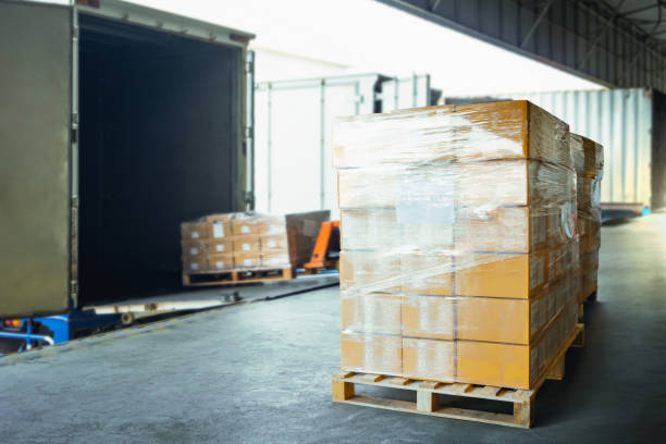 Image of a pallet of boxes wrapped up in plastic film ready to be loaded onto a delivery truck with other pallets being loaded in the background