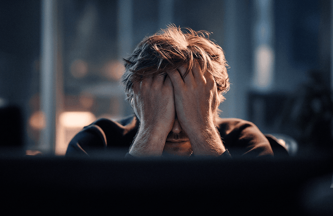 Um homem com as mãos no rosto, parecendo estressado em um escritório.