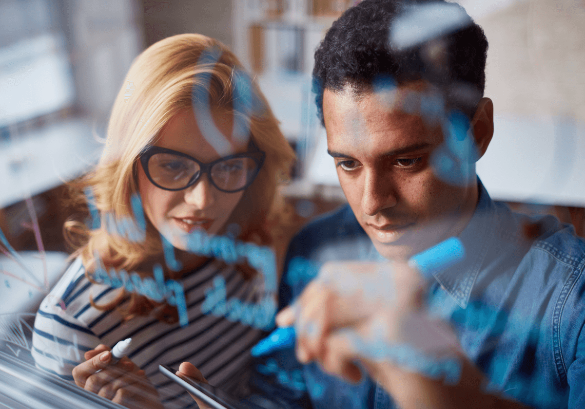 Smiling young woman with long hair standing against a dark green background, holding a finger to her chin.