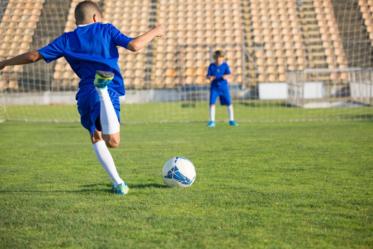 man in white soccer jersey kicking soccer ball on green grass field during daytime